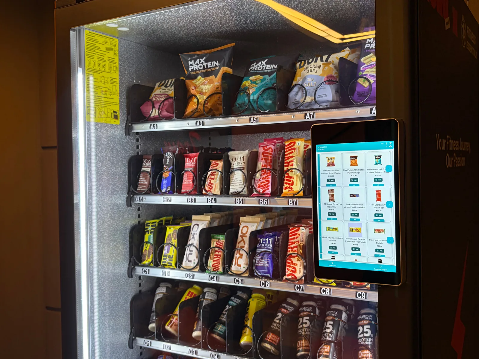 The payment tablet on a Zoruvend machine showing the on-screen product menu with prices, beside the stocked shelves it lists