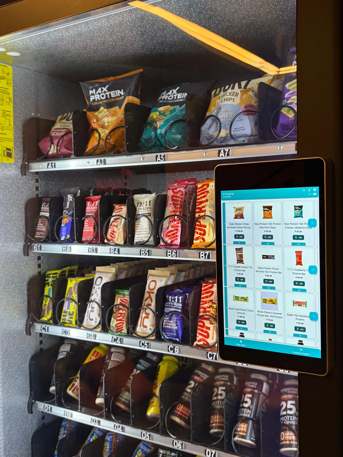 Close view of packaged protein snacks held in the coiled trays of a Zoruvend machine, each row labelled with its selection code